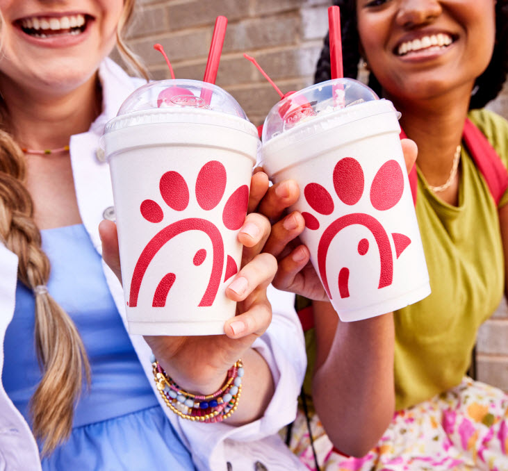Two people smiling and clinking together Chick-fil-A milkshakes