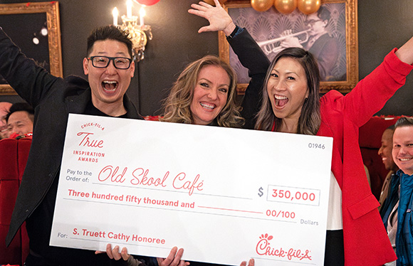 A women from the S. Truett Cathy Honoree, Old Skool Café, holding a large check and standing next to two other people
