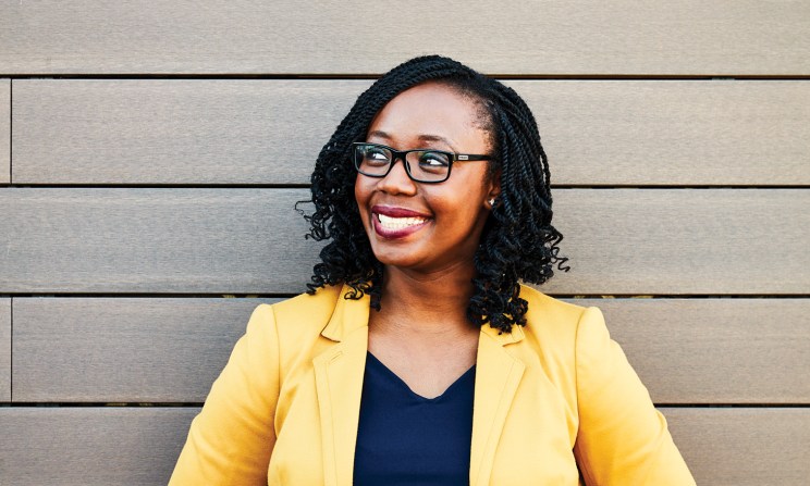 Woman in a yellow blazer smiling in front of wooden panels.