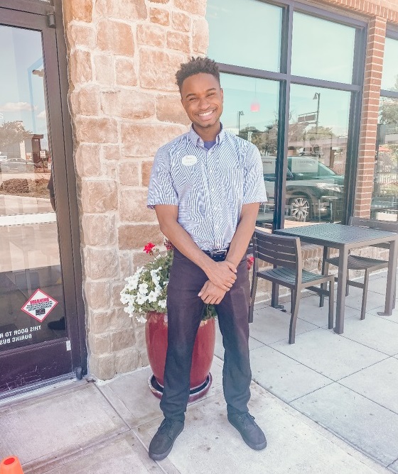 A smiling Chick-fil-A team member in outside of the restaurant.