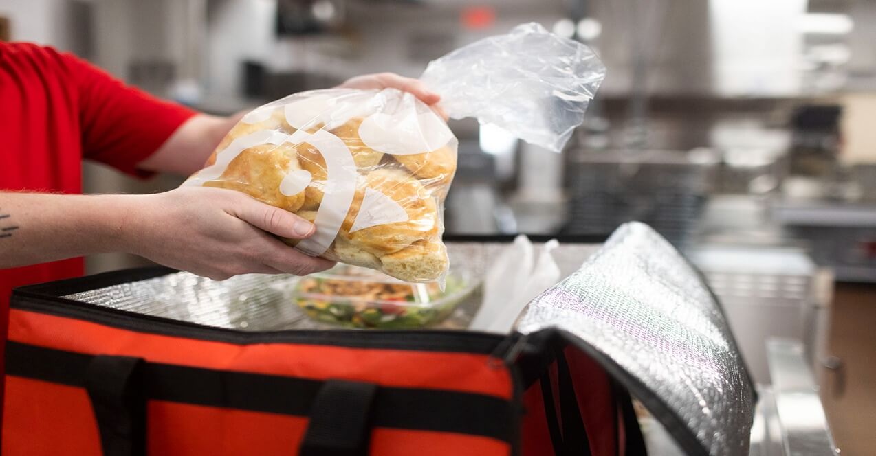 Person placing a sealed bag of Chick-fil-A biscuits into an insulated red catering bag in a kitchen setting.