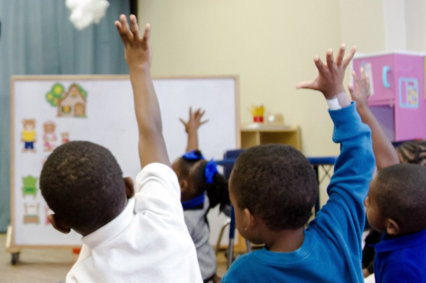 Young children in a classroom raising their hands
