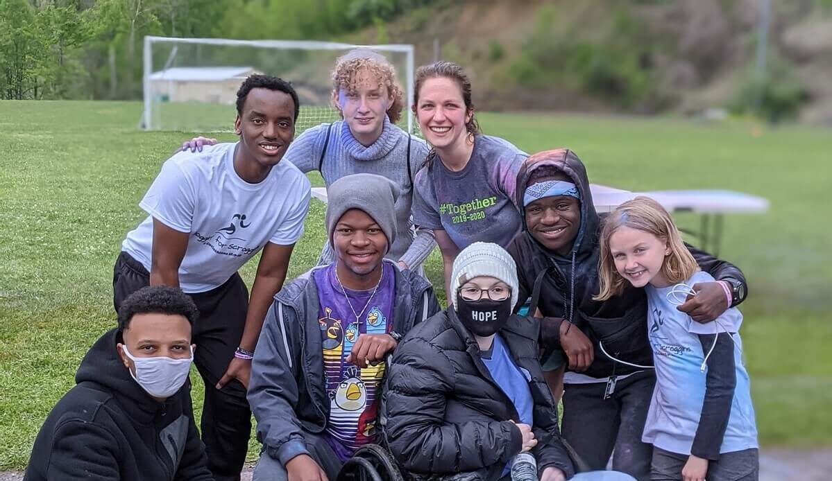 A group of eight people happily posing together outdoors on a grassy field.