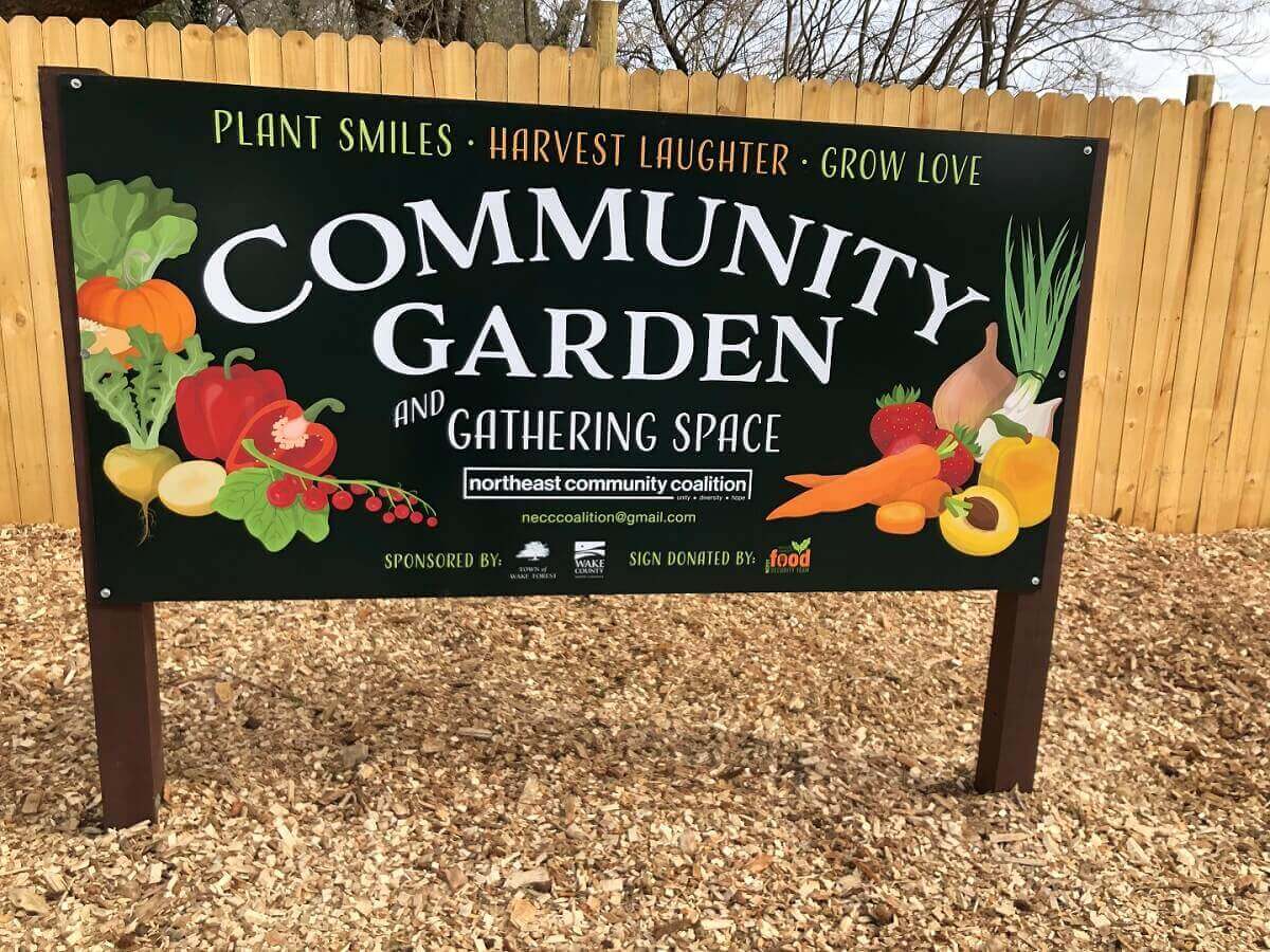 Community garden sign with illustrations of various vegetables and fruits against a wooden fence, saying PLANT SMILES • HARVEST LAUGHTER • GROW LOVE
COMMUNITY GARDEN AND GATHERING SPACE