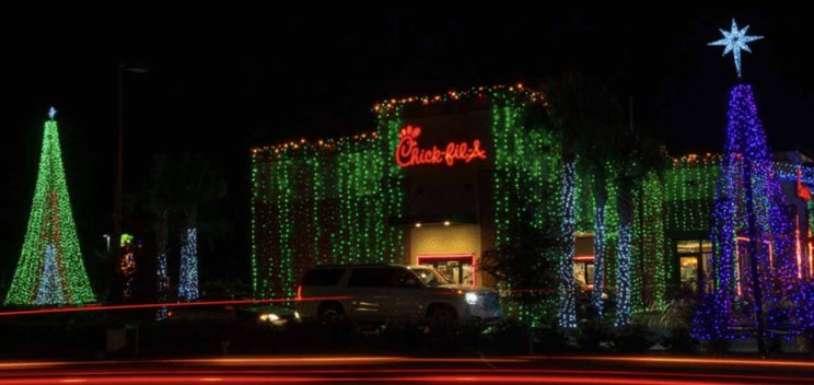 A Chick-fil-A restaurant decorated with colorful Christmas lights and lighted tree displays at night.