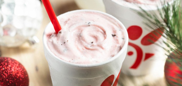 Holiday-themed scene with a peppermint milkshake in a Chick-fil-A cup, surrounded by festive decorations.