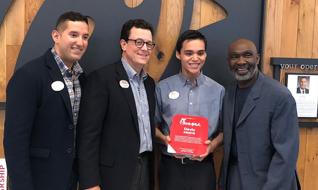 Four men posing together, one holding a red Chick-fil-A plaque.