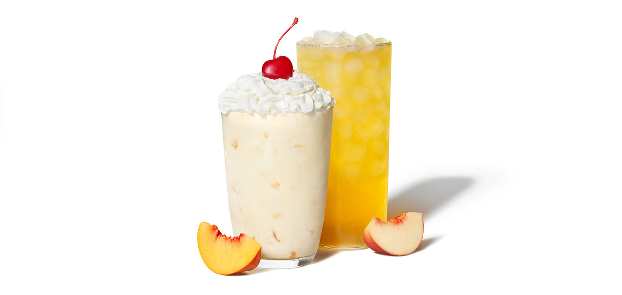 A peach milkshake and a pach lemonade in glasses, surrounded by fresh peach slices.
