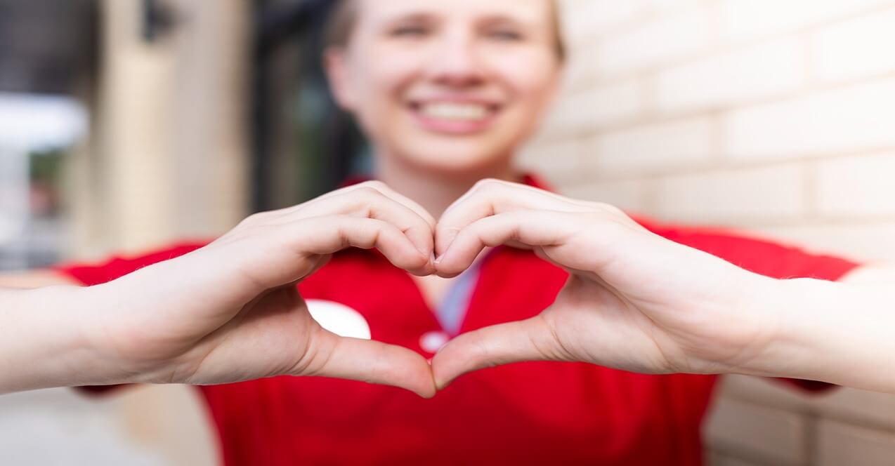 Smiling Chick-fil-A Team Member forming a heart shape with hands in front of their chest.