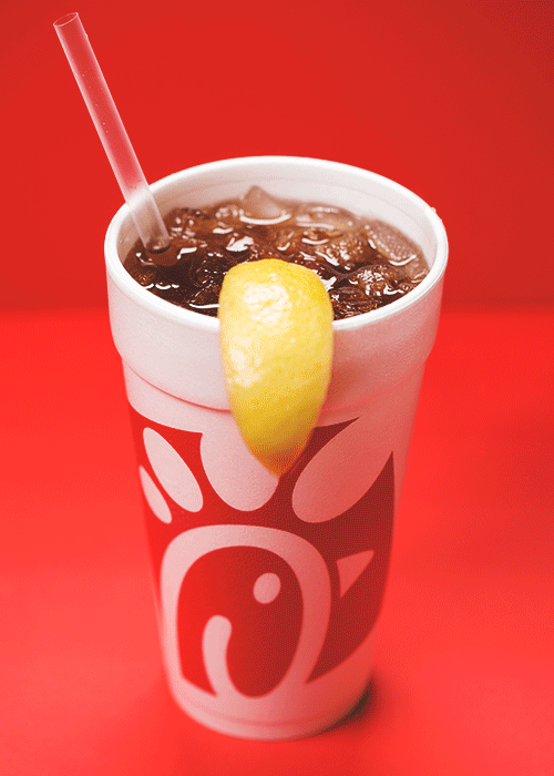 Chick-fil-A iced tea in a foam cup with a lemon wedge and straw spinning against  a red background.








