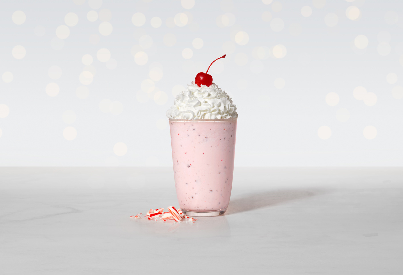 Broken candy canes next to a Peppermint shake with festive lights in the background.