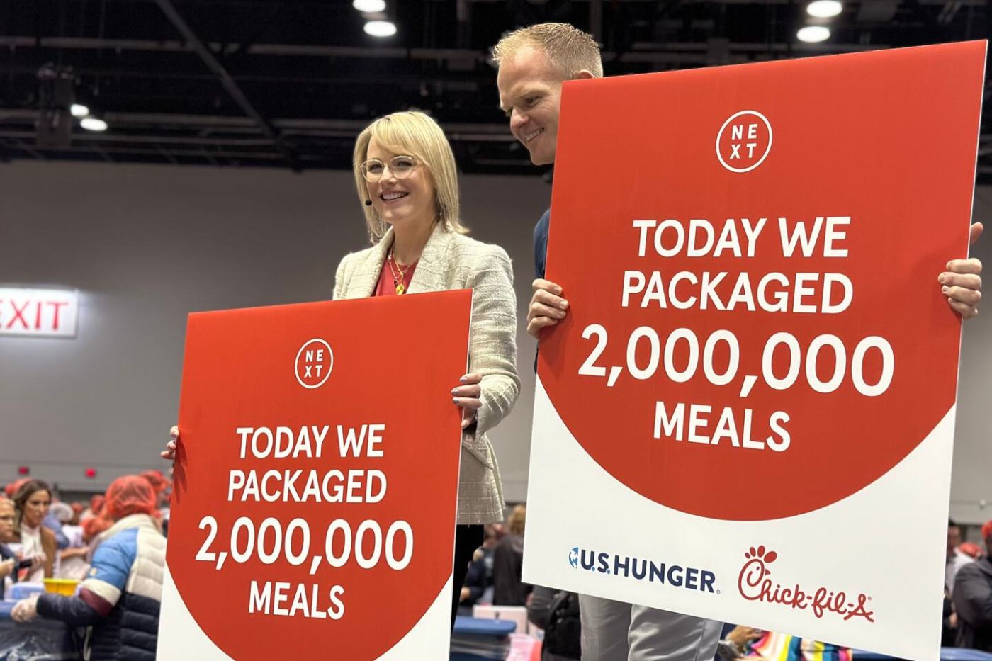 Two people holding signs that read "Today We Packaged 2,000,000 Meals" at a meal-packing event.