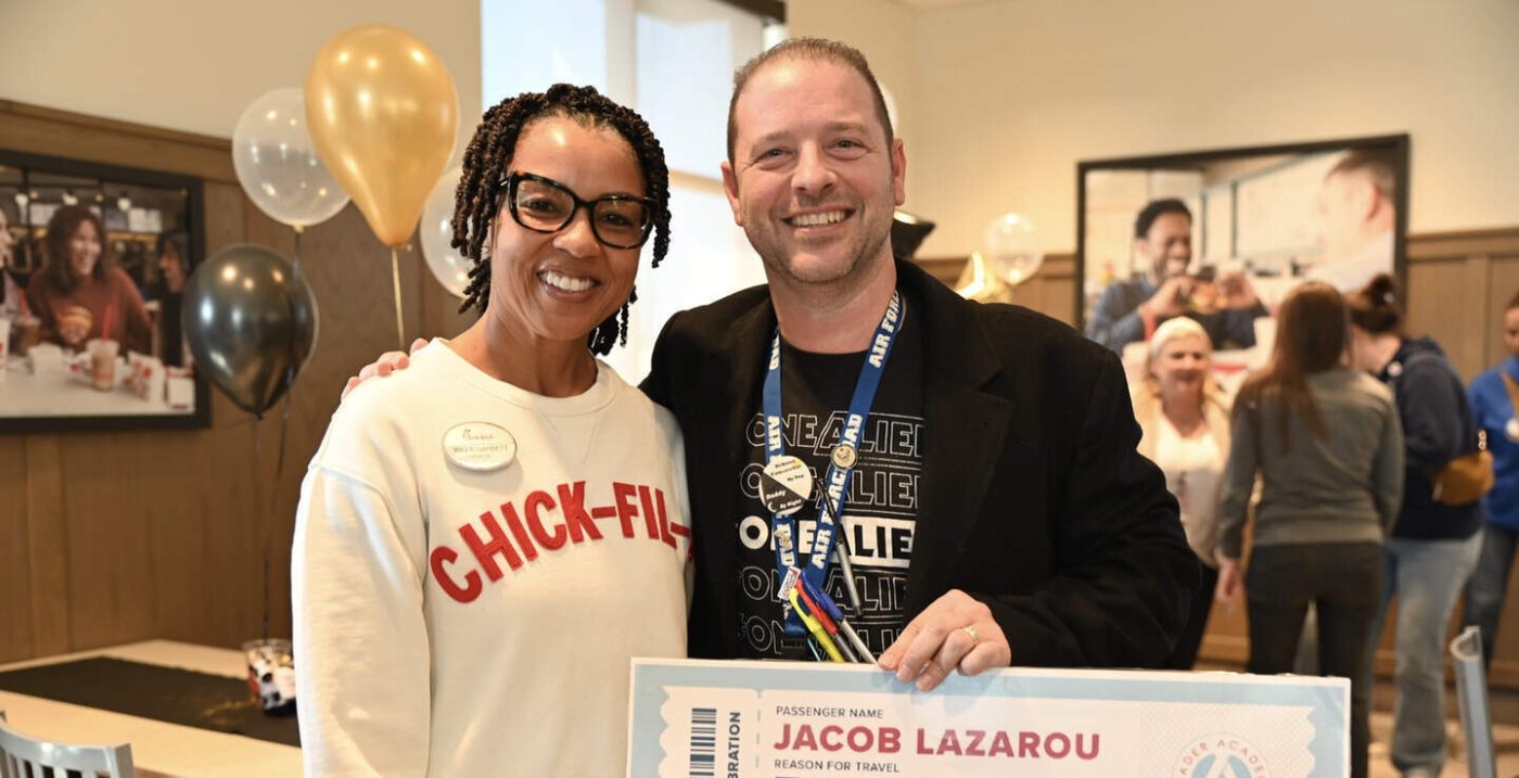 Two people smiling, one in a "CHICK-FIL-A" shirt and the other holding a large boarding pass.