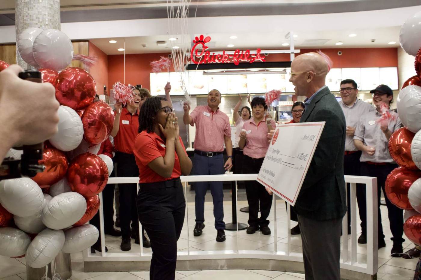 A team member receives a scholarship check while her team members celebrate with balloons and streamers.