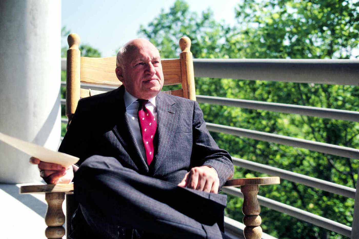 S. Truett Cathy sitting in a rocking chair outside and holding a paper.