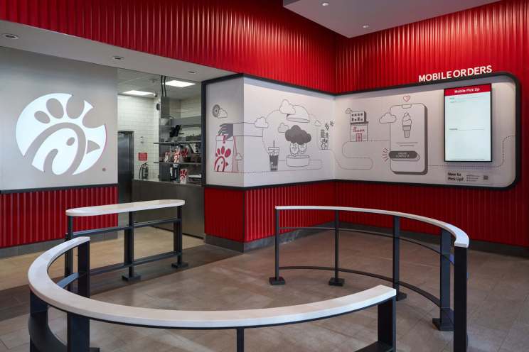 Mobile pickup area in a with red walls, open kitchen, and illustrated wall with a digital screen for orders.