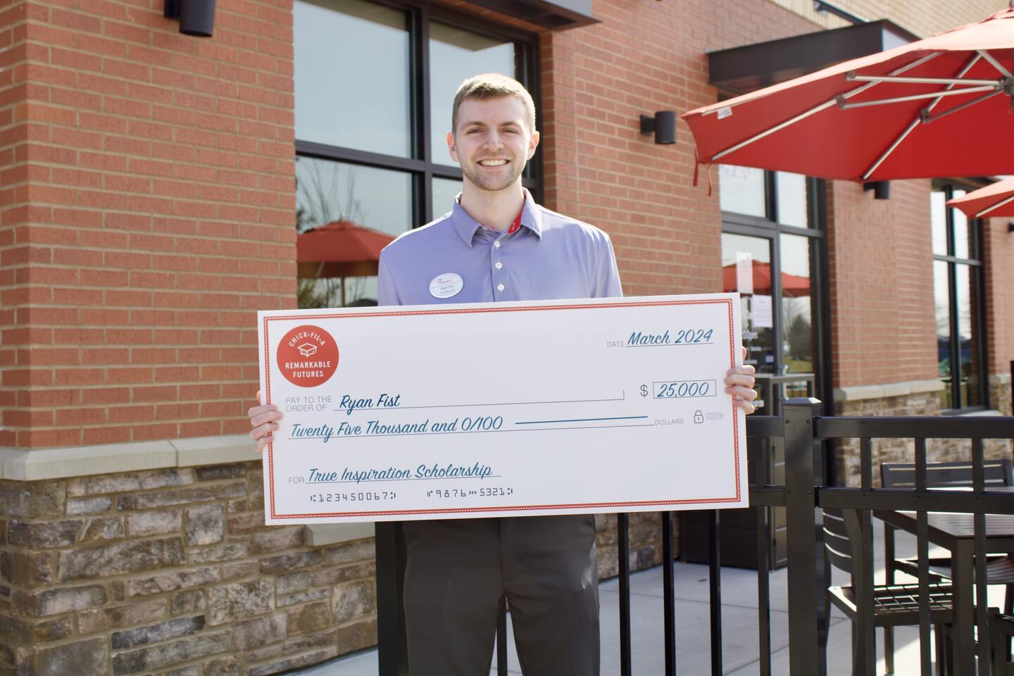 A team member holds an oversized check outside of Chick-fil-A.
