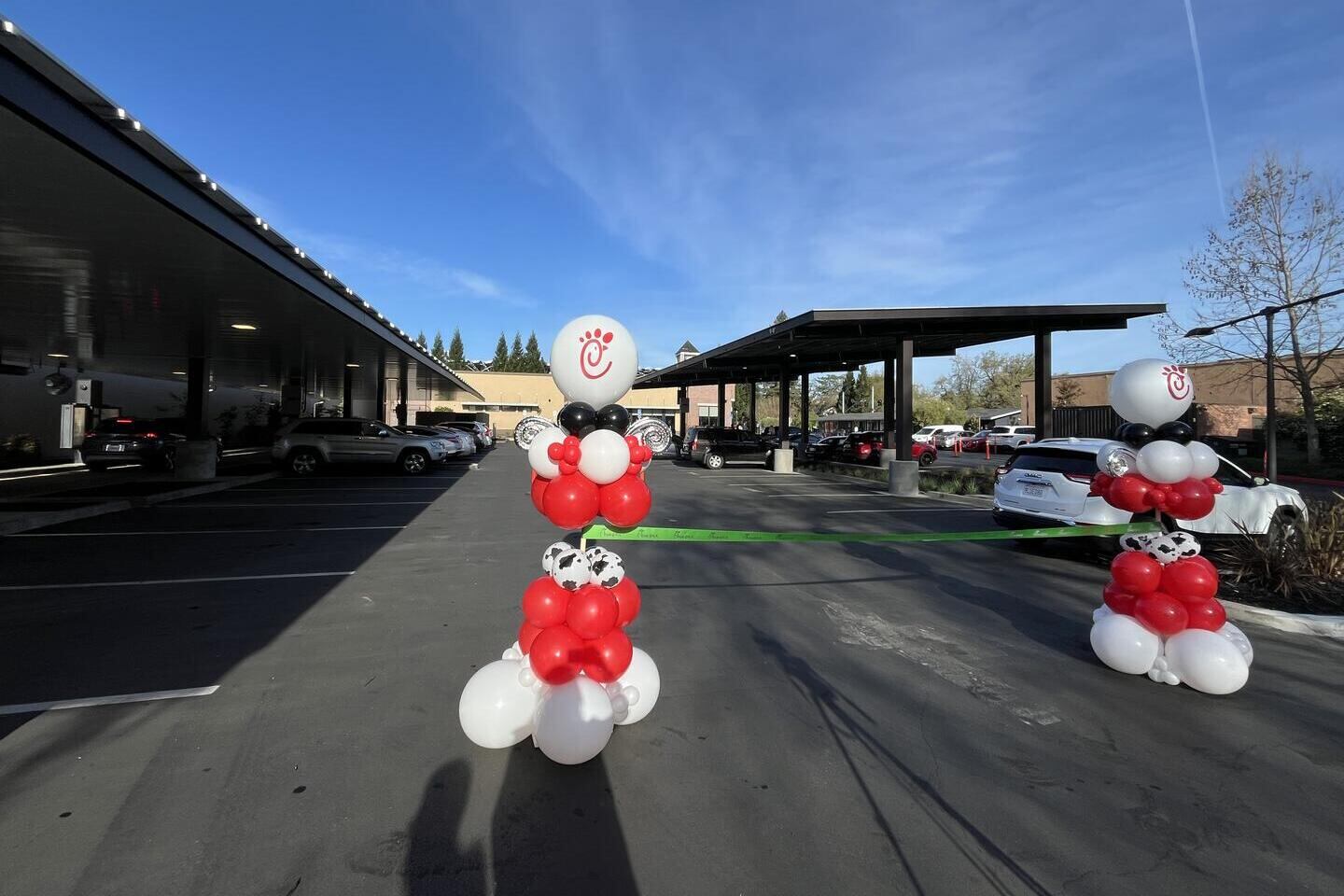 Balloon columns with a green ribbon in the parking lot, under blue skies.

