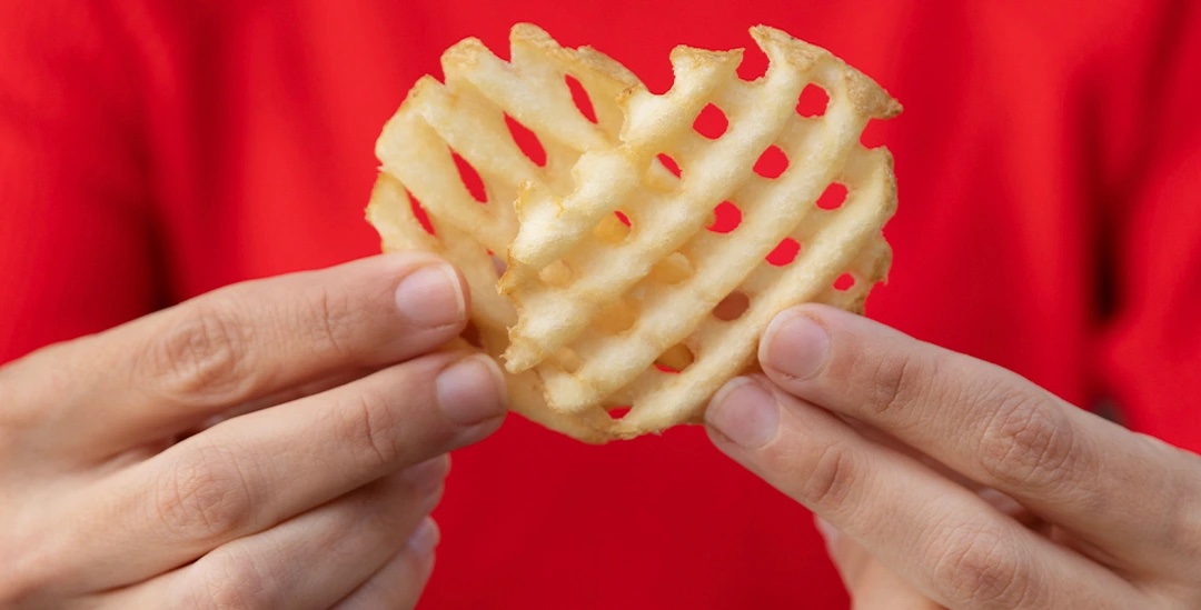 Waffle-cut fry in the shape of a heart held by two hands.