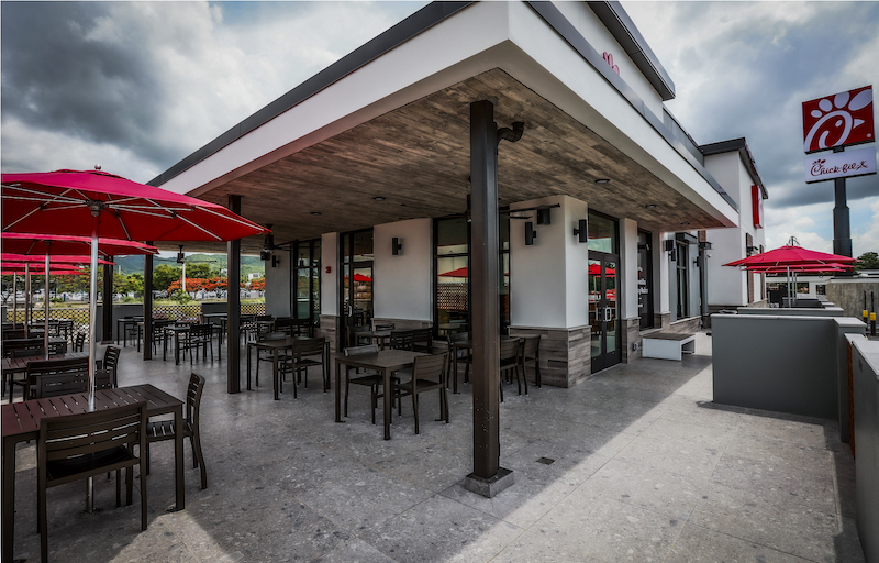 Outdoor Chick-fil-A restaurant seating area with tables, chairs, and red umbrellas.

