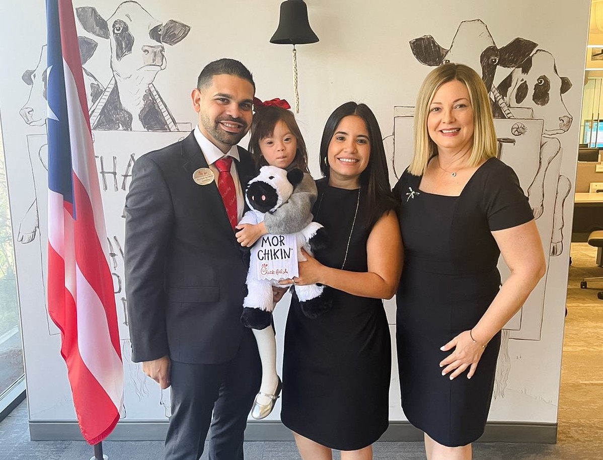 Enrique Questell Pereira stands with two women and a young girl holding a Chick-fil-A cow plush toy.