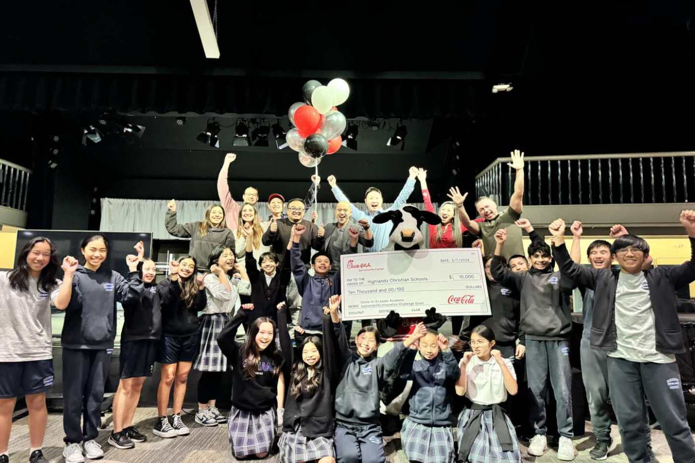 Students at the Highlands Christina Schools cheer while a Chick-fil-A mascot holds an oversized check.