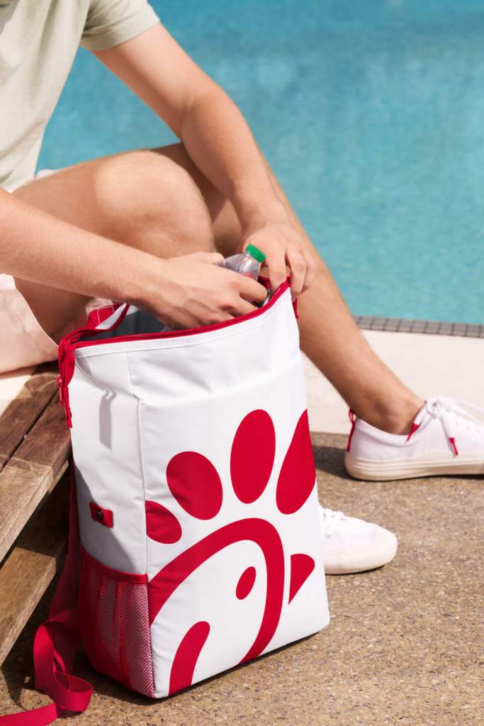 Person sitting by a pool places a water bottle into a white cooler backpack with a large red Chick-fil-A logo.
