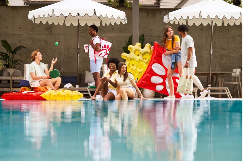 A group of young people enjoying a sunny day by a pool, surrounded by playful inflatable toys and a white umbrella.