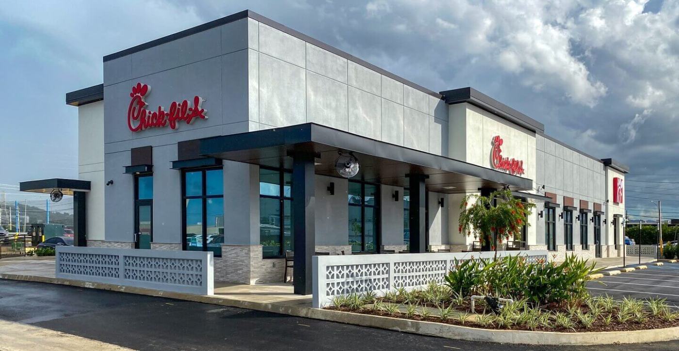 Exterior of a modern Chick-fil-A restaurant with drive-thru lanes and landscaped surroundings, under a cloudy sky.