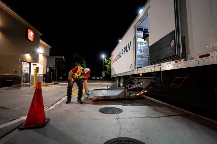 Delivery worker adjusts a ramp of a supply truck at night outside a restaurant.