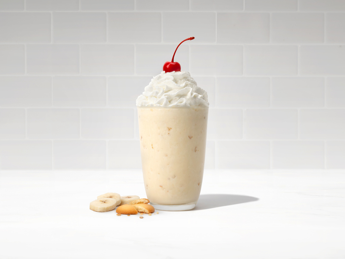 Banana Pudding Milkshake in a glass on a wooden board surrounded by ingredients 