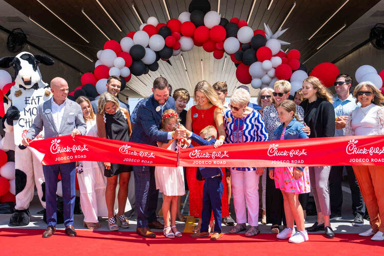 A Chick-fil-A ribbon-cutting ceremony with people cutting a red ribbon under a balloon arch.