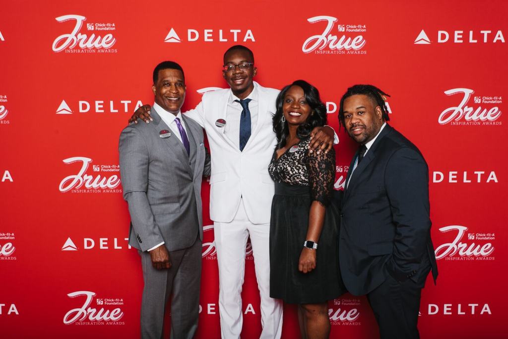 Four people standing in front of a red Chick-fil-A Foundation and Delta backdrop, wearing formal attire.