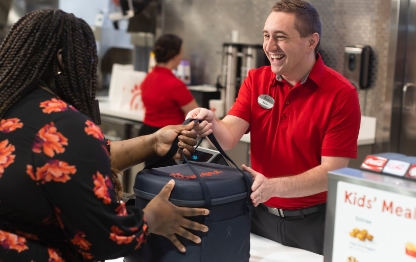 A Team Member smiling and handing a Customer an insulated Chick-fil-A bag.