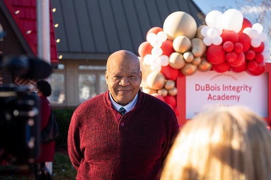 A man stands in front of a "DuBois Integrity Academy" sign adorned with balloons.