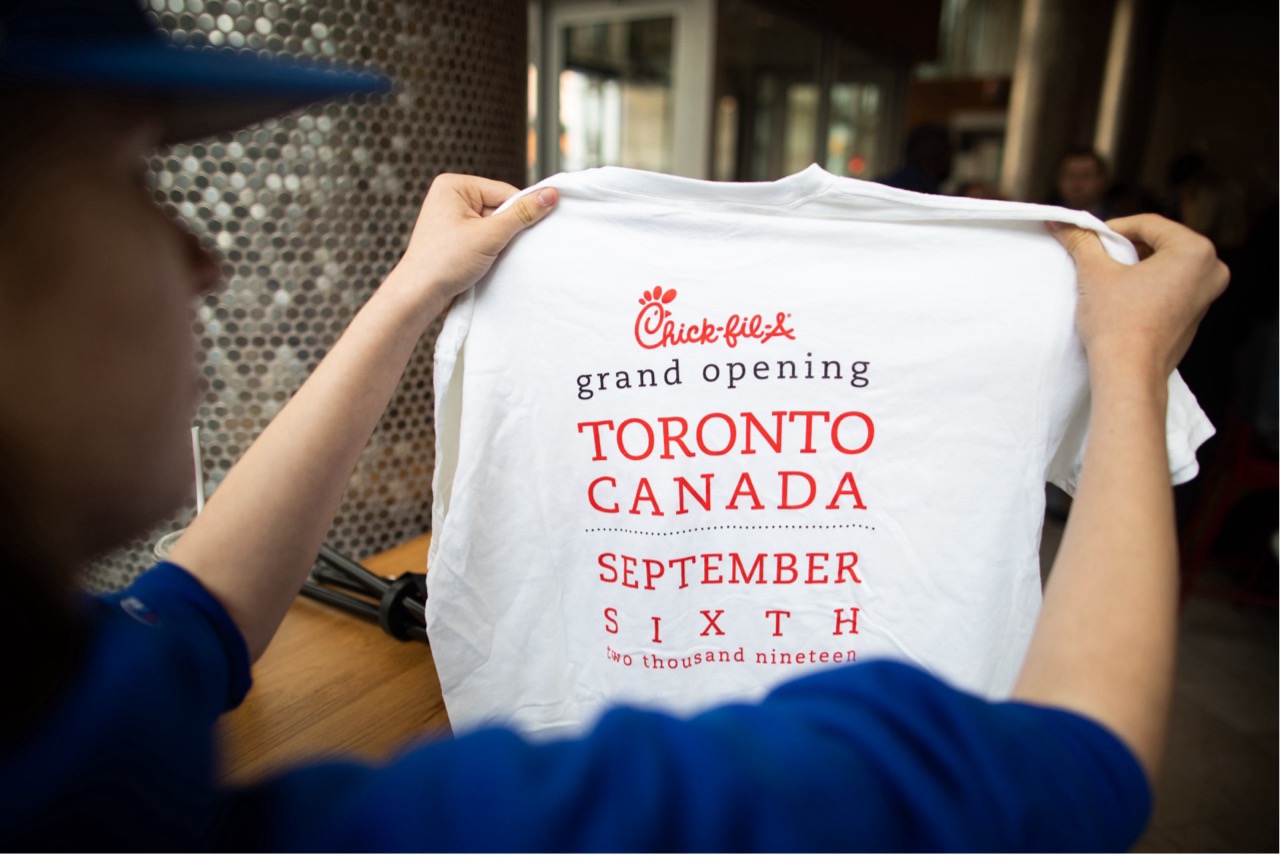 Person holding a white Chick-fil-A t-shirt promoting the grand opening in Toronto, Canada on September 6, 2019.