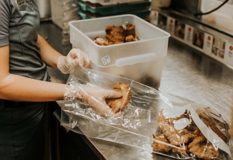 A team member placing cooked chicken in plastic bag for donation.