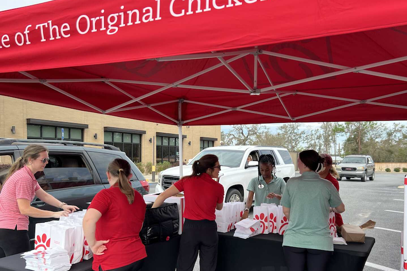 Chick-fil-A team members prepare and distribute meals under a red tent in a parking lot for hurricane relief.