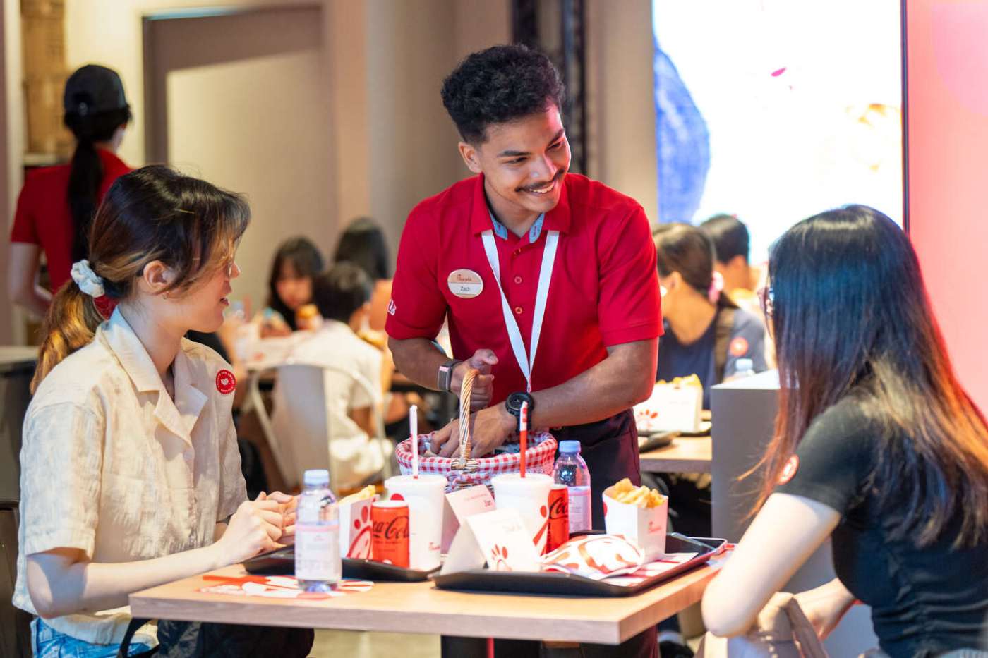 A smiling Chick-fil-A Team member talking with two customers seated at a table.