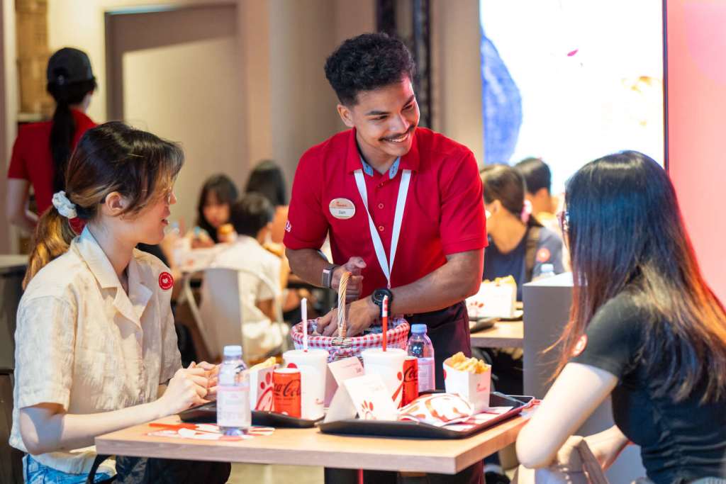 A smiling Chick-fil-A Team member talking with two customers seated at a table.