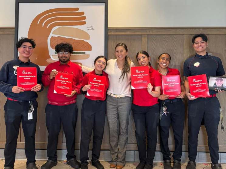 Six people, five in Chick-fil-A uniforms, holding "Remarkable Futures Scholar" certificates, standing indoors with a sandwich graphic in the background.