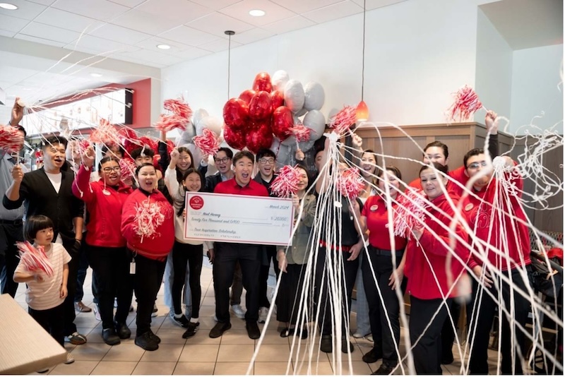 A group of Chick-fil-A team members celebrate indoors with pom-poms, balloons, and streamers as one person holds a large check.