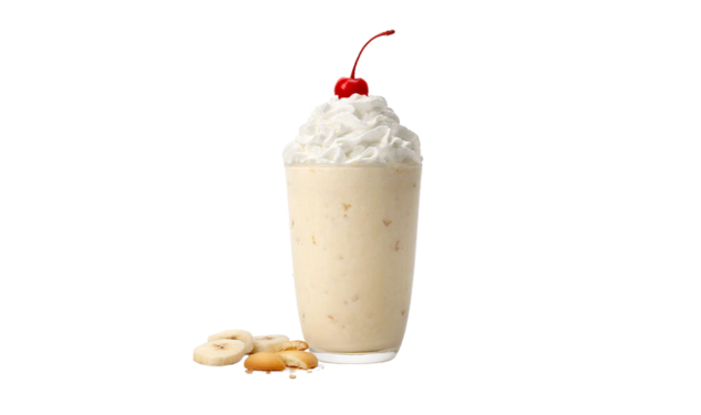 A banana pudding milkshake with whipped cream and a cherry on top, surrounded by banana slices and cookies.