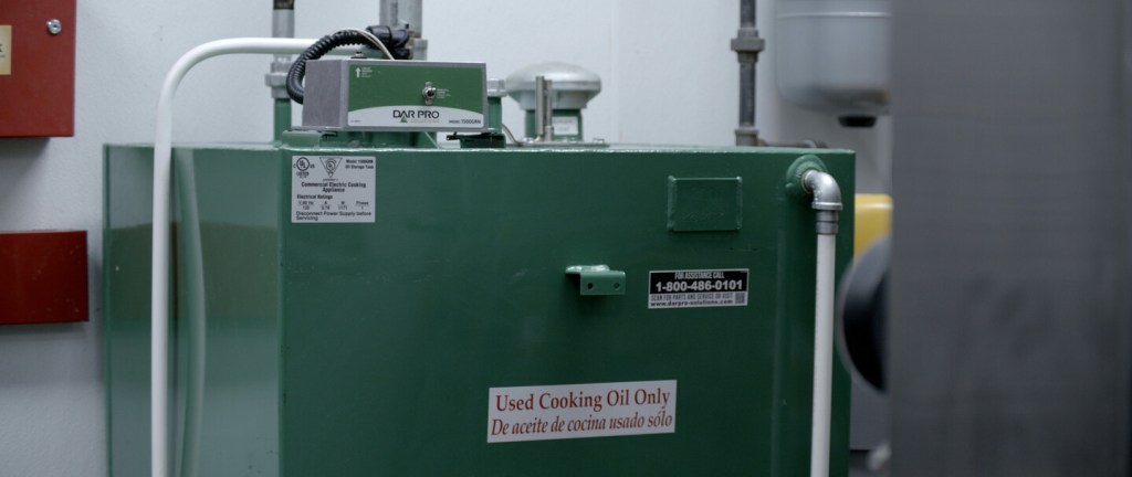 Green oil storage tank with pipes and warning labels indoors.