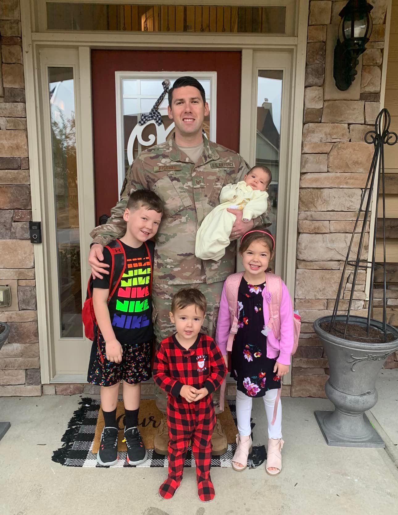 A man in a U.S. Air Force uniform standing on a porch with his four young children.