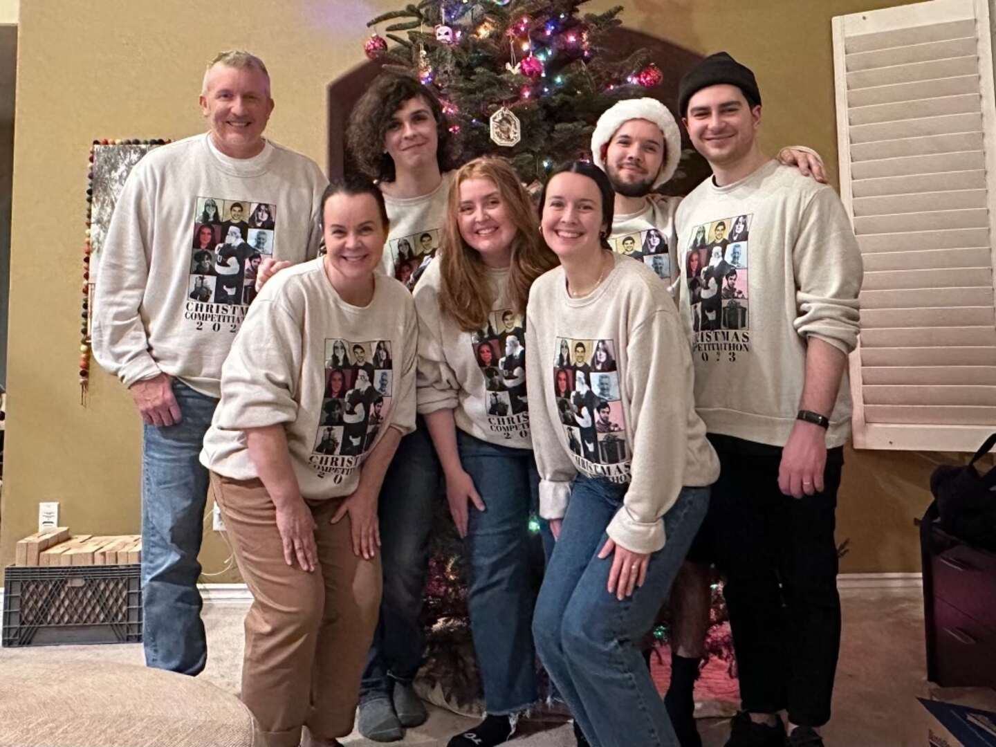 Kasi Corbett poses with her husband and children in matching Christmas sweatshirts in front of a decorated tree.