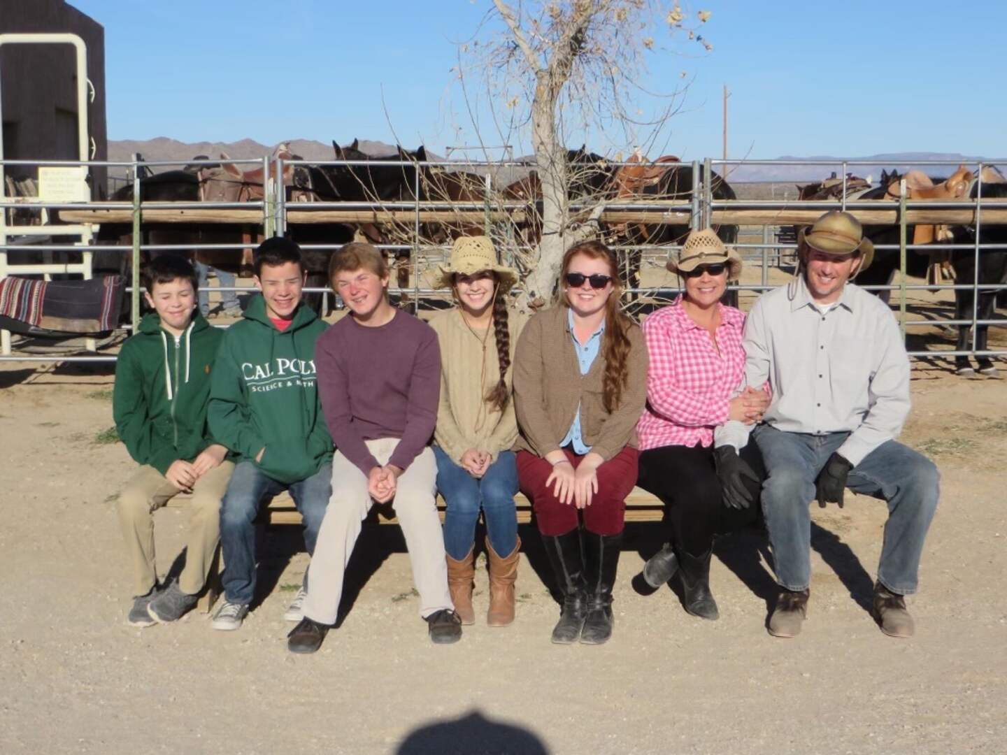 Kasi Corbett and her family sit together on a bench at a ranch, with horses and fencing in the background.