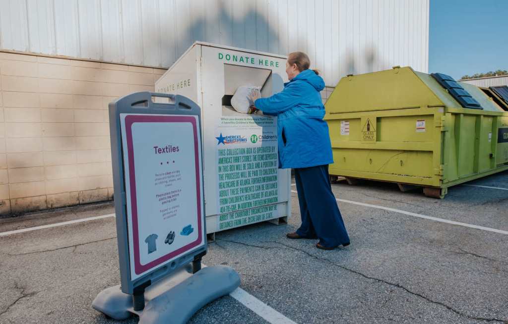 A person donates a bag of textiles into a donation bin.