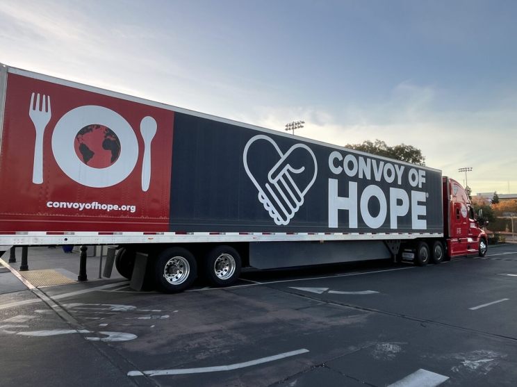 A truck trailer displaying Convoy of Hope branding, featuring a globe plate and heart-fork graphic.
