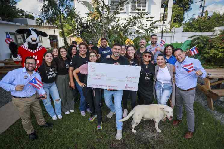 Group of people, including the Chick-fil-A cow mascot, celebrate outdoors as they hold a large $200,000 check awarded to Happy Givers.